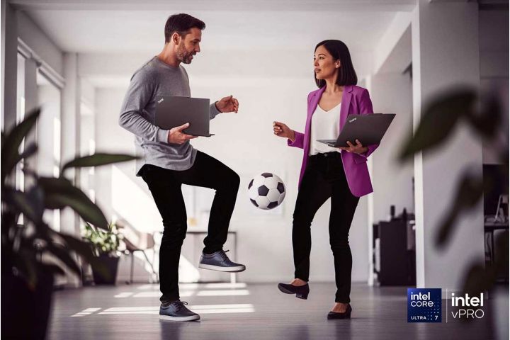 Two colleagues standing in a hallway and kicking a soccer ball back and forth.