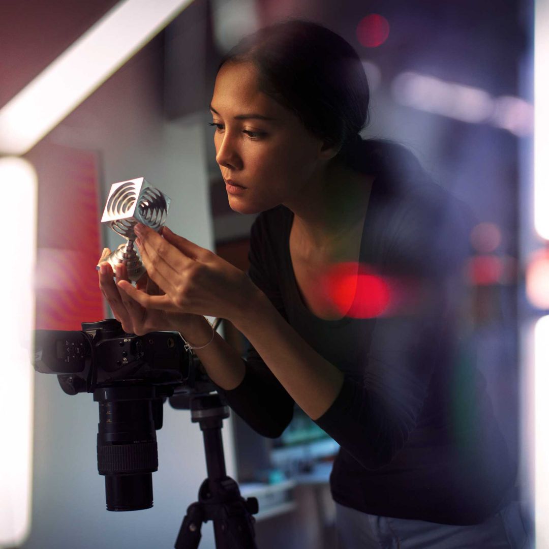 A woman with a camera on an easel examining a metal object in her hands.