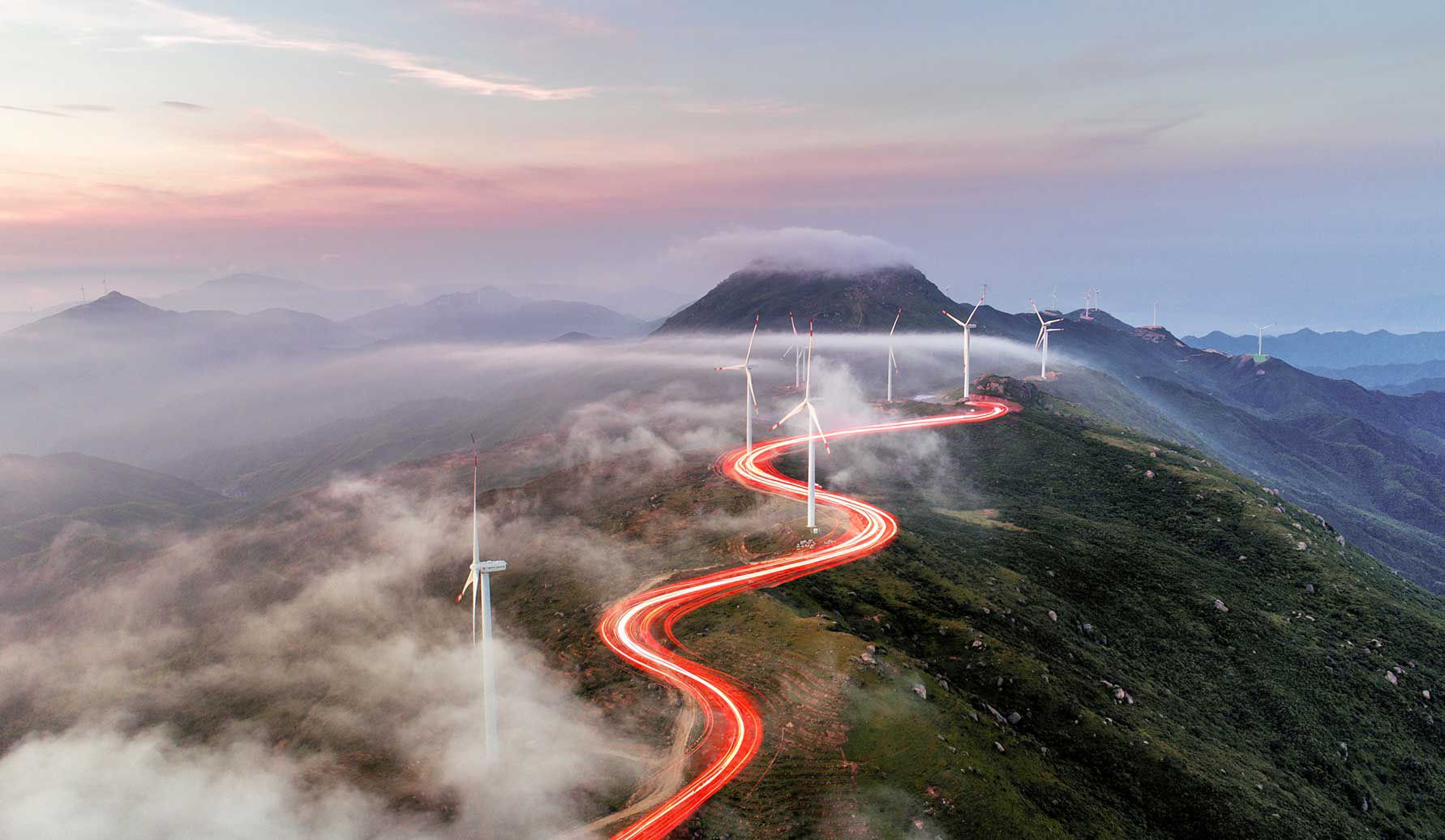 Un éclairage rouge traversant les éoliennes sur les sommets des collines.