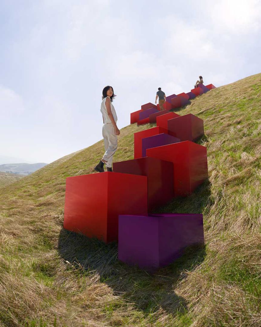 Des cubes rouges et pourpres montant une colline herbeuse avec trois personnes qui les montent.