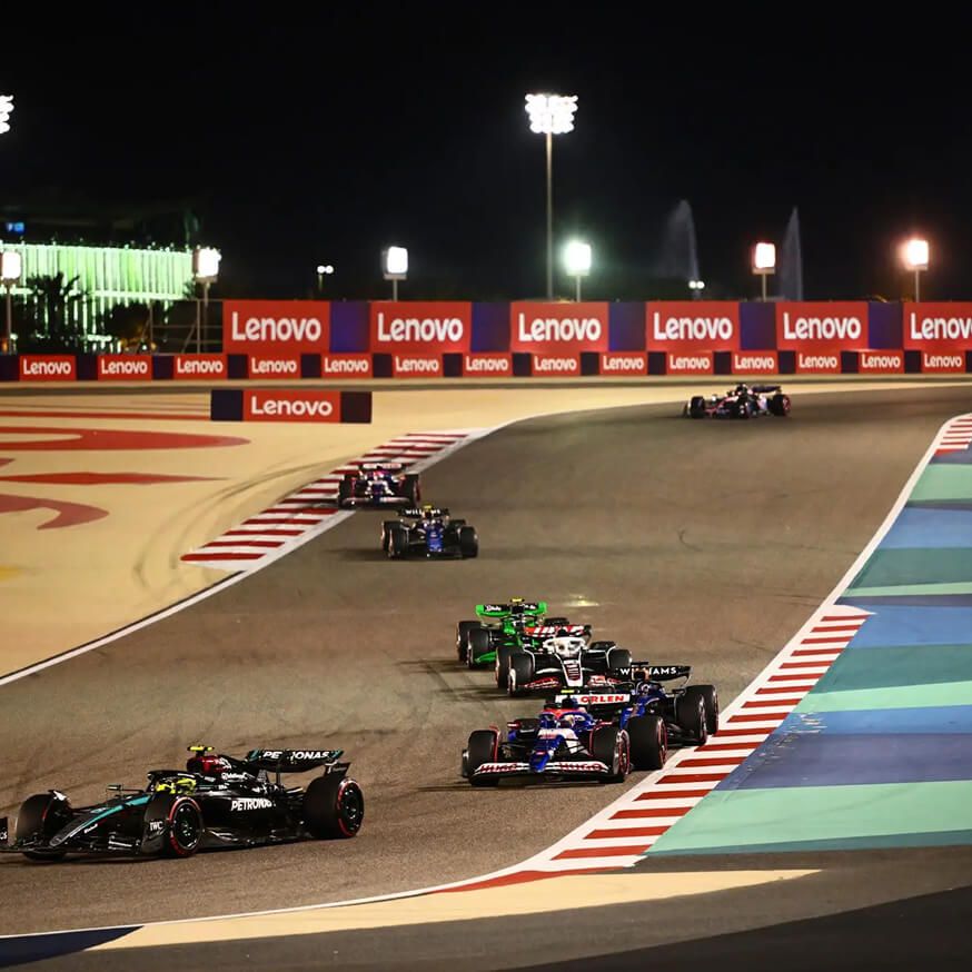 Voitures de Formule 1® courant sur une piste la nuit, affichage Lenovo en arrière-plan.