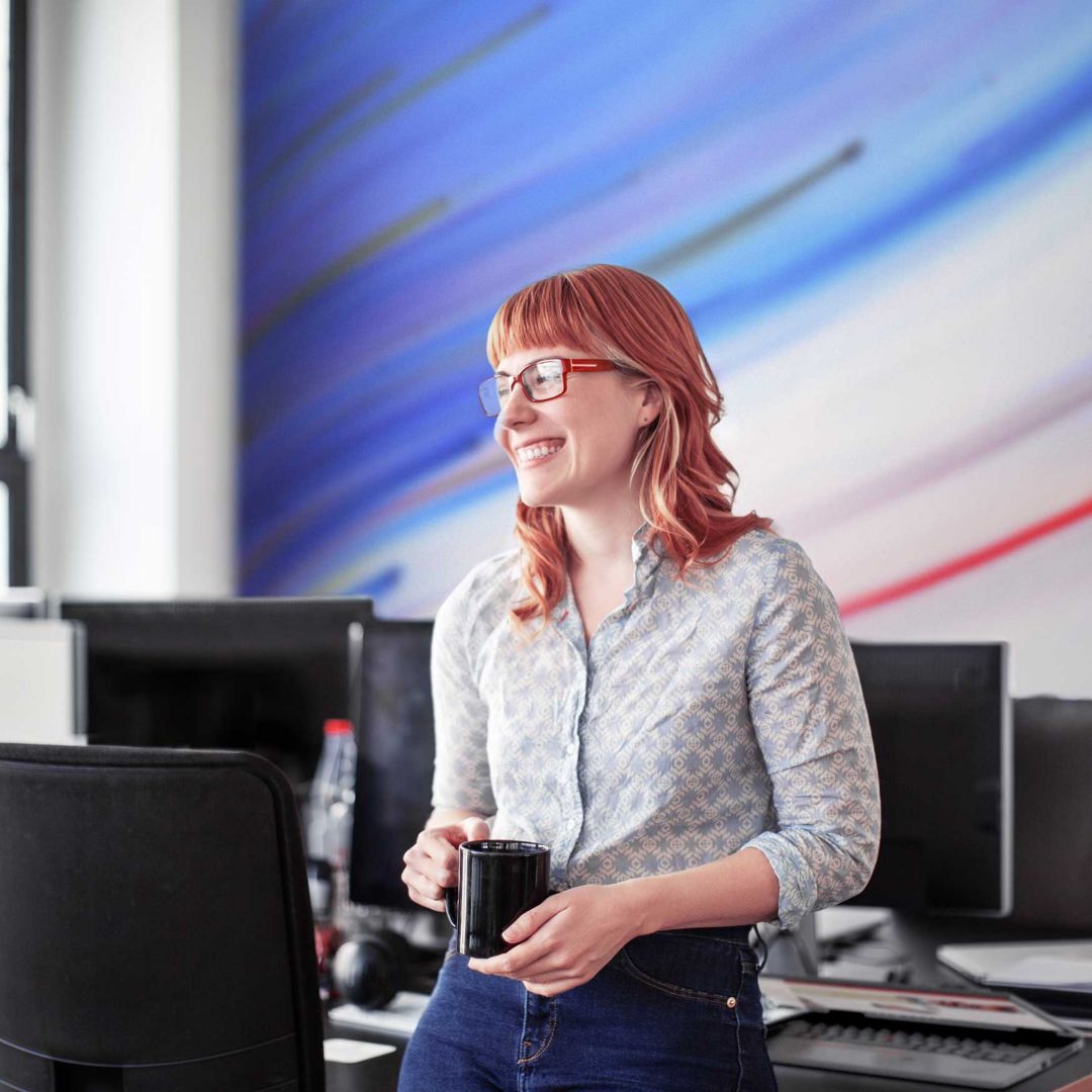 Une femme souriante tenant une tasse de café et étudiant à un bureau au bureau.