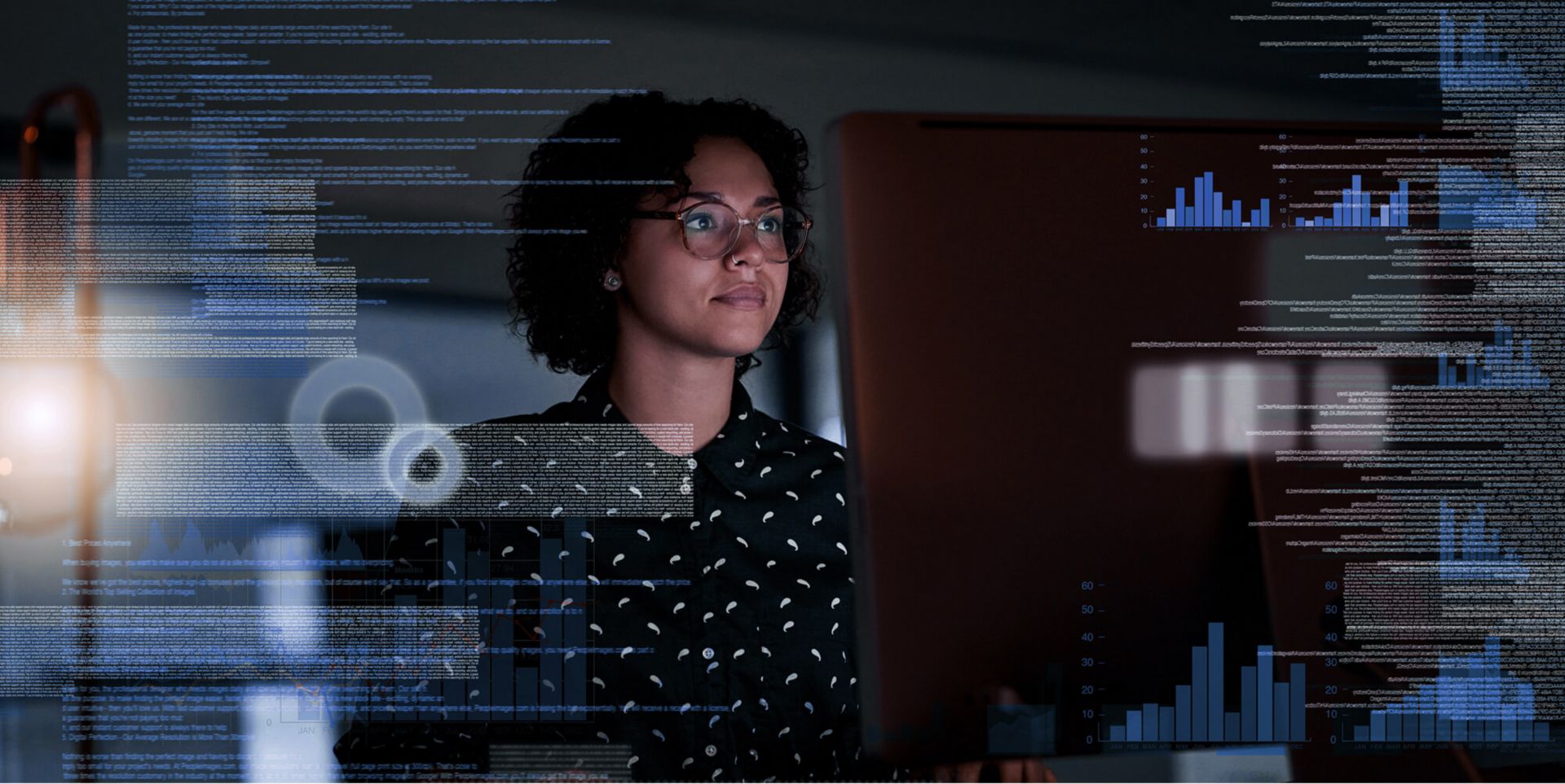 A woman looking at a big monitor, the data from the screen reflecting over top of her.