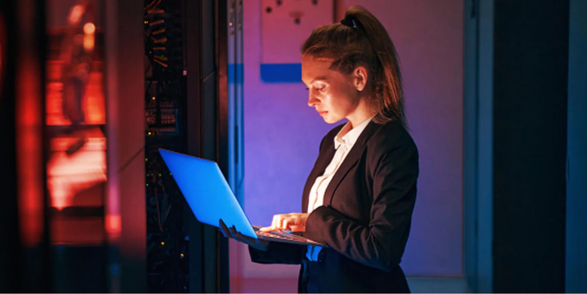 A woman using a laptop in a server room.