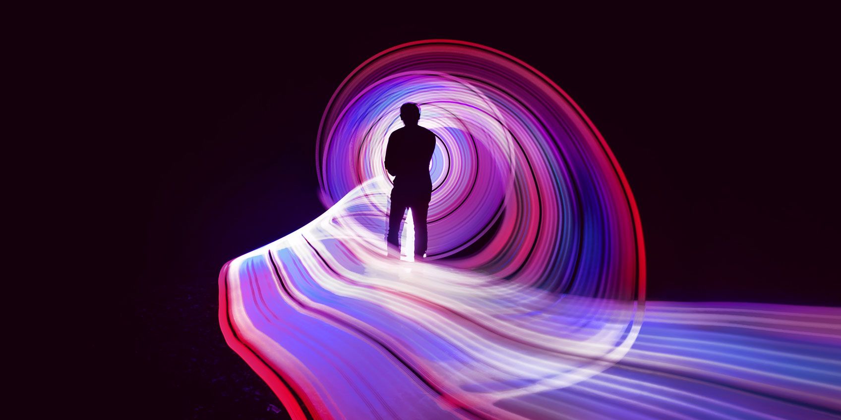 A silhouette of a person in the center of an abstract swirl of red and purple light. 