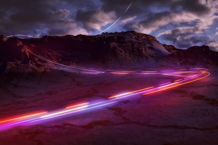Time-lapsed traffic lines ascend a curving mountain road.