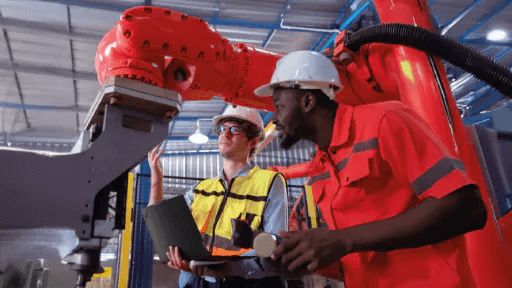 Two co-workers collaborating using laptops and looking at a machine