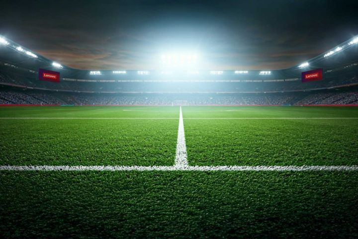 An empty soccer pitch with a stadium full of fans at night.
