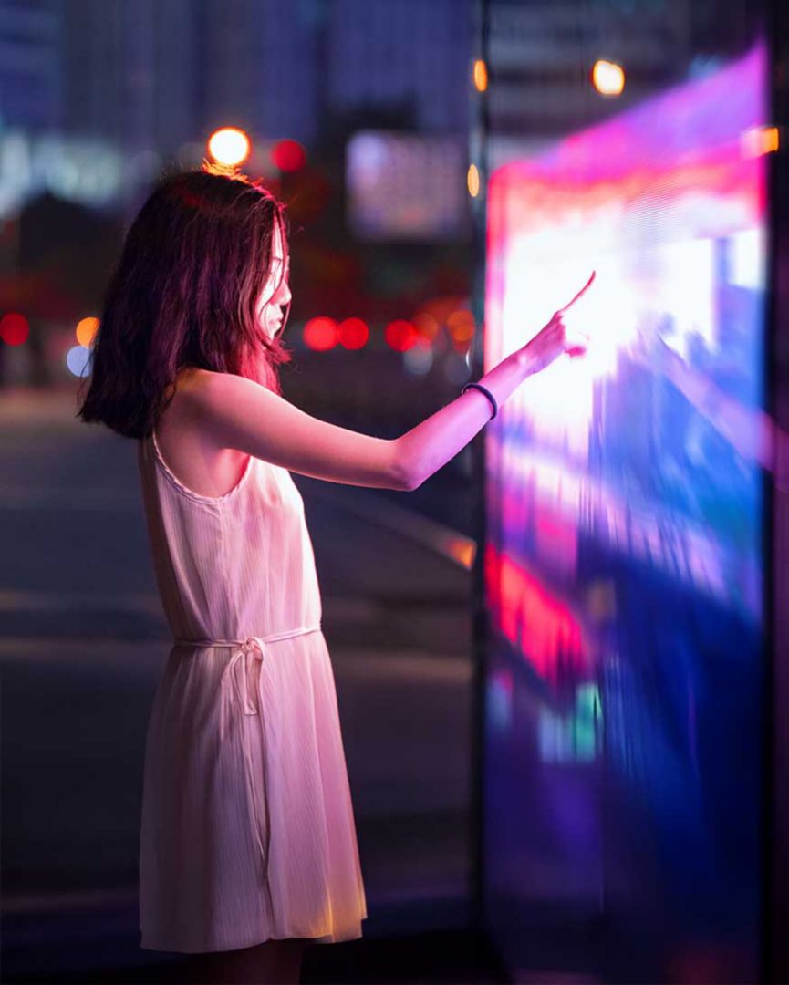 A girl using a touchscreen at night on a city street. 