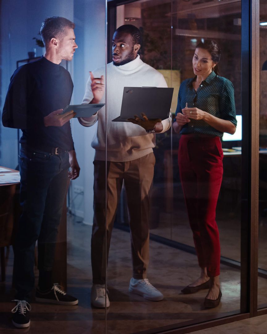 Three colleagues standing and looking at the laptop and tablet in their hands.