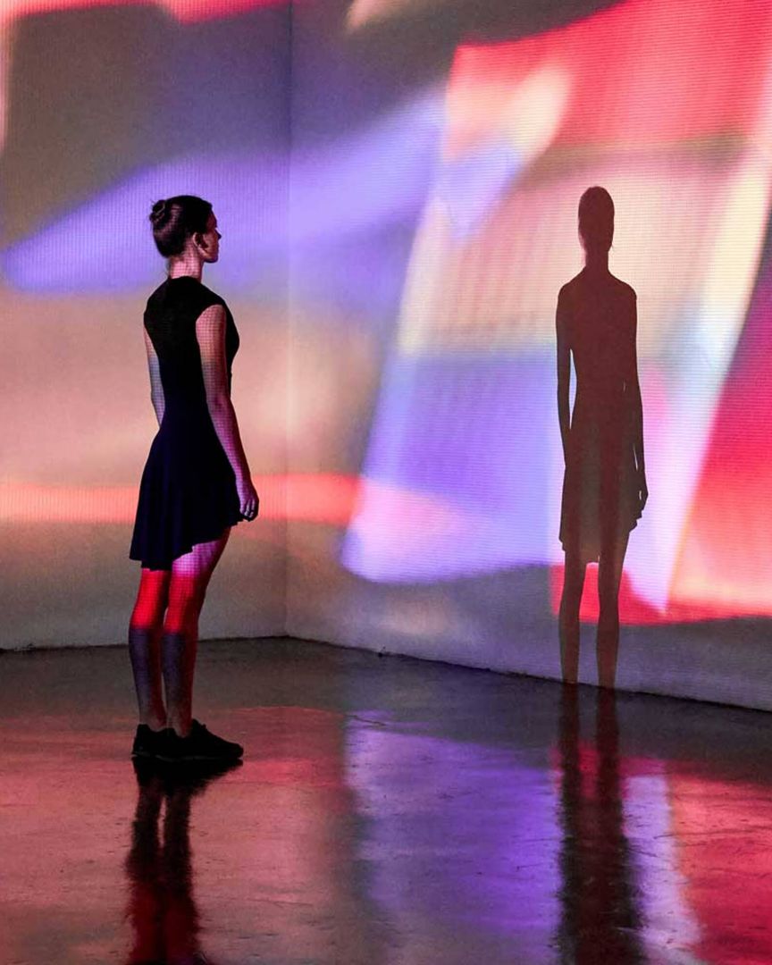 A woman staring at her shadow on a colorful wall.