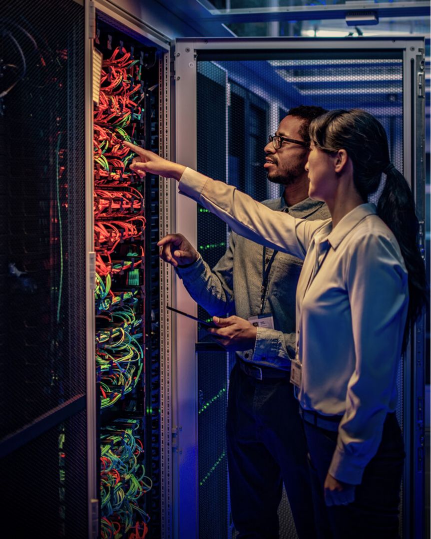 Two colleagues inspecting the cables in the back of a server.