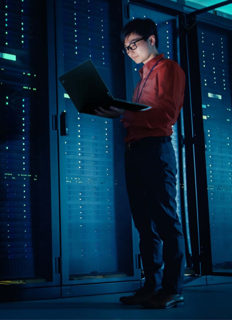 A man looking at his laptop in a dark server room.