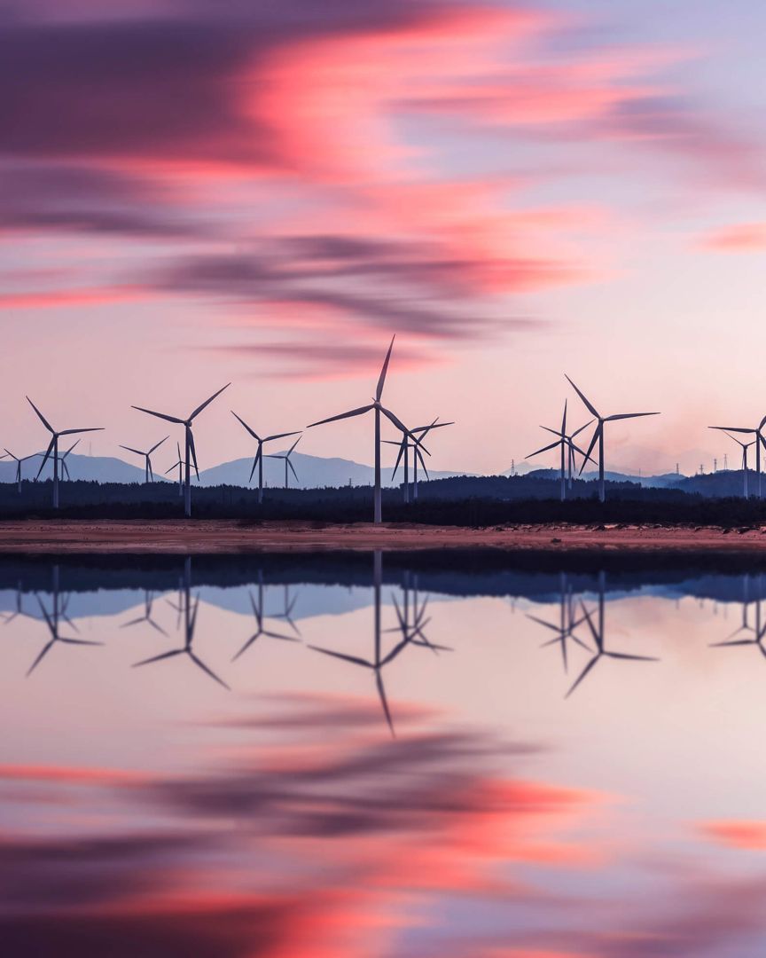 Turbines at dusk reflecting onto a lake.