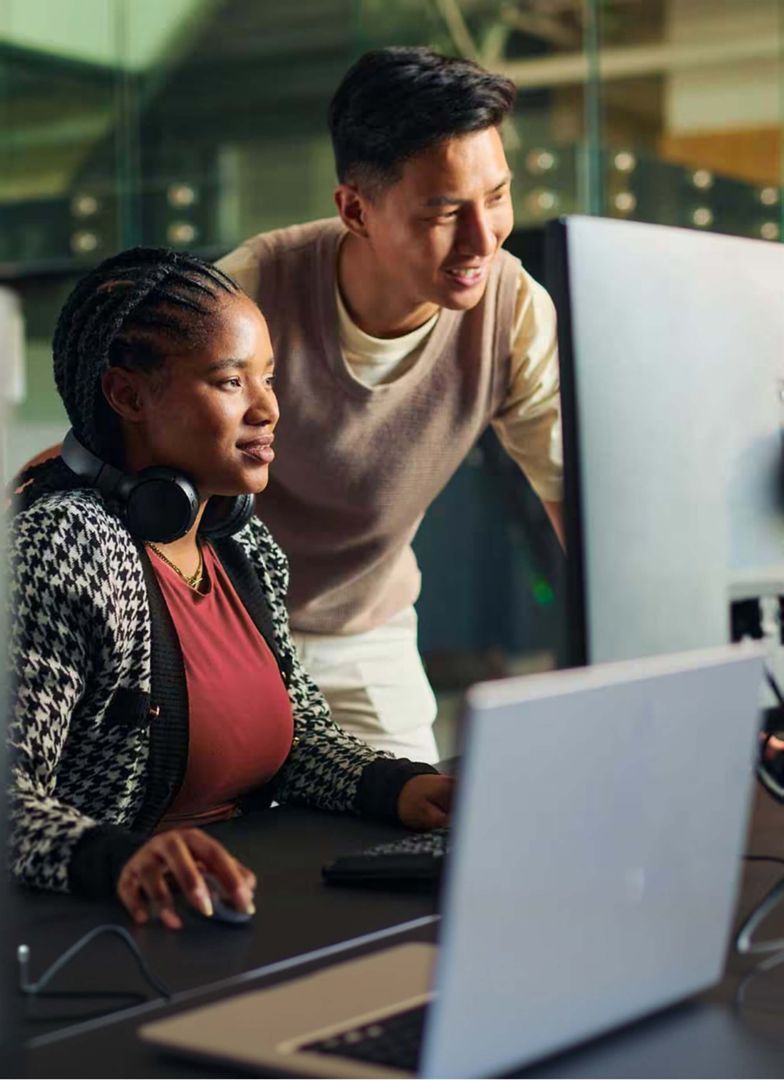 A colleague hoovering over a colleague’s shoulder, pointing to her screen.