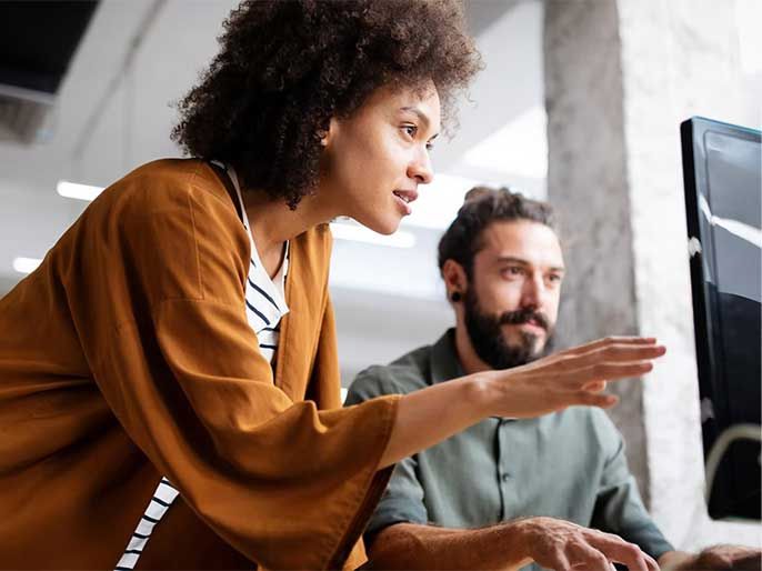 A female colleague helping her male colleague on his computer.