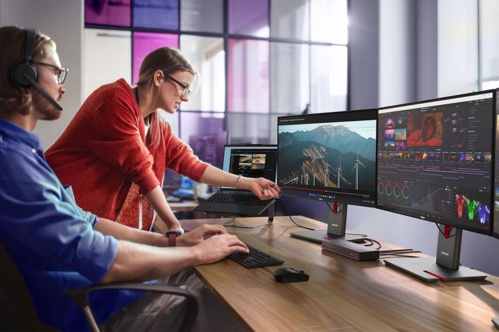 A woman pointing at a man’s middle monitor as they collaborate on content creation.  