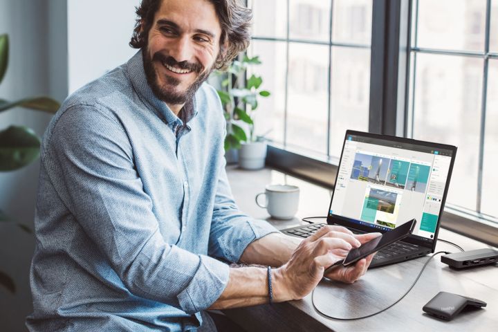 A man at his desk with his laptop and typing on his phone.  
