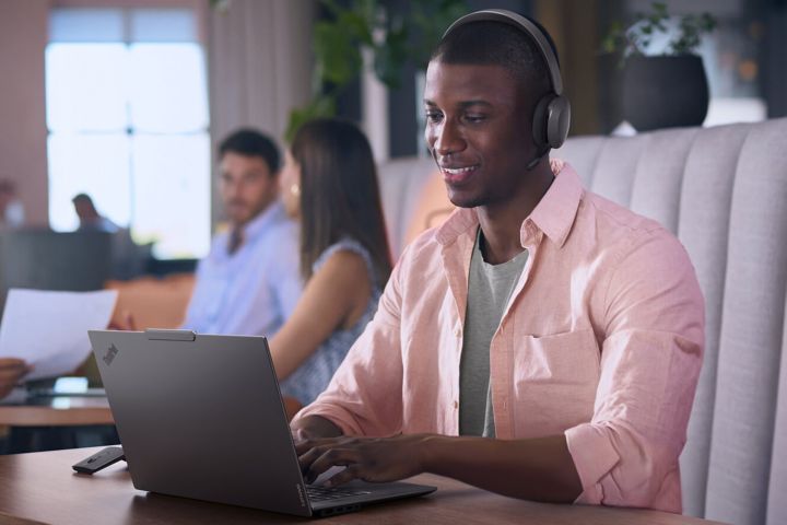 A man in an open office typing on his laptop and wearing headphones. 