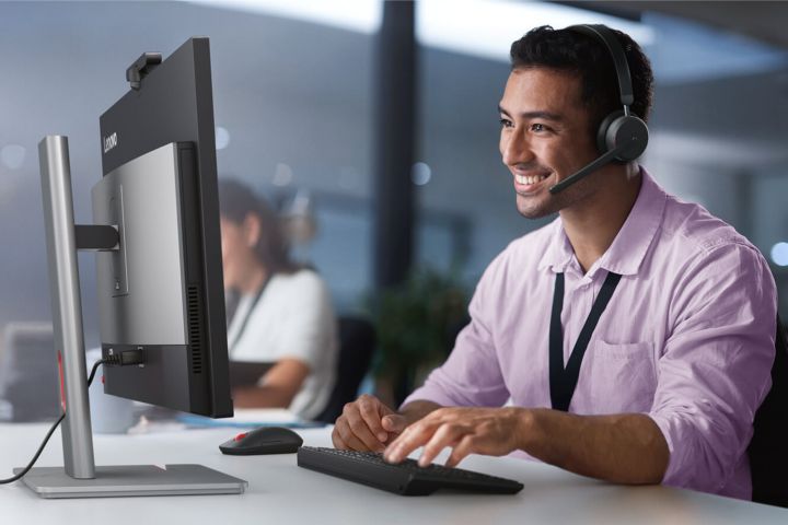 An IT professional wearing a headset and smiling at his computer. 