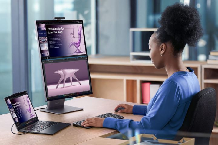 A woman working with a vertical monitor, AI PC laptop, keyboard, and mouse.