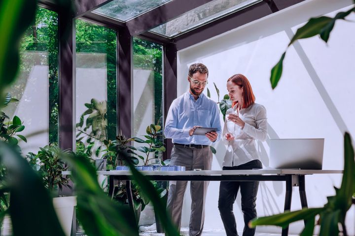 Two people collaborating on a tablet in a room with a glass ceiling and wall.