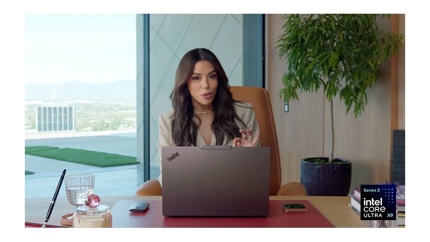 Seated at a desk and wearing a power suit, Eva Longoria makes the OK sign with her fingers behind a Lenovo ThinkPad laptop