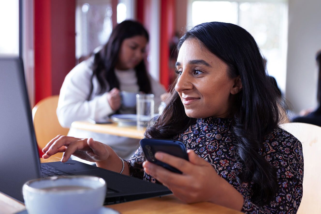 Mulher usando seu telefone para inserir informações em seu notebook. — Atualizado na página global