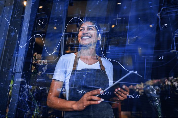 A woman holding a tablet and looking at her reflection on a screen showing a graph.