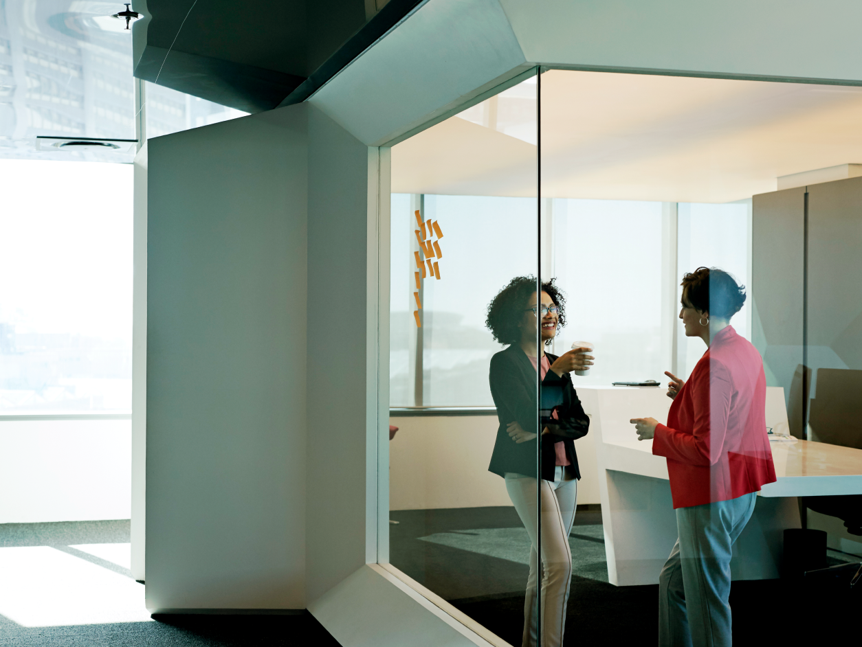 Two colleagues talking in a glass-walled office.
