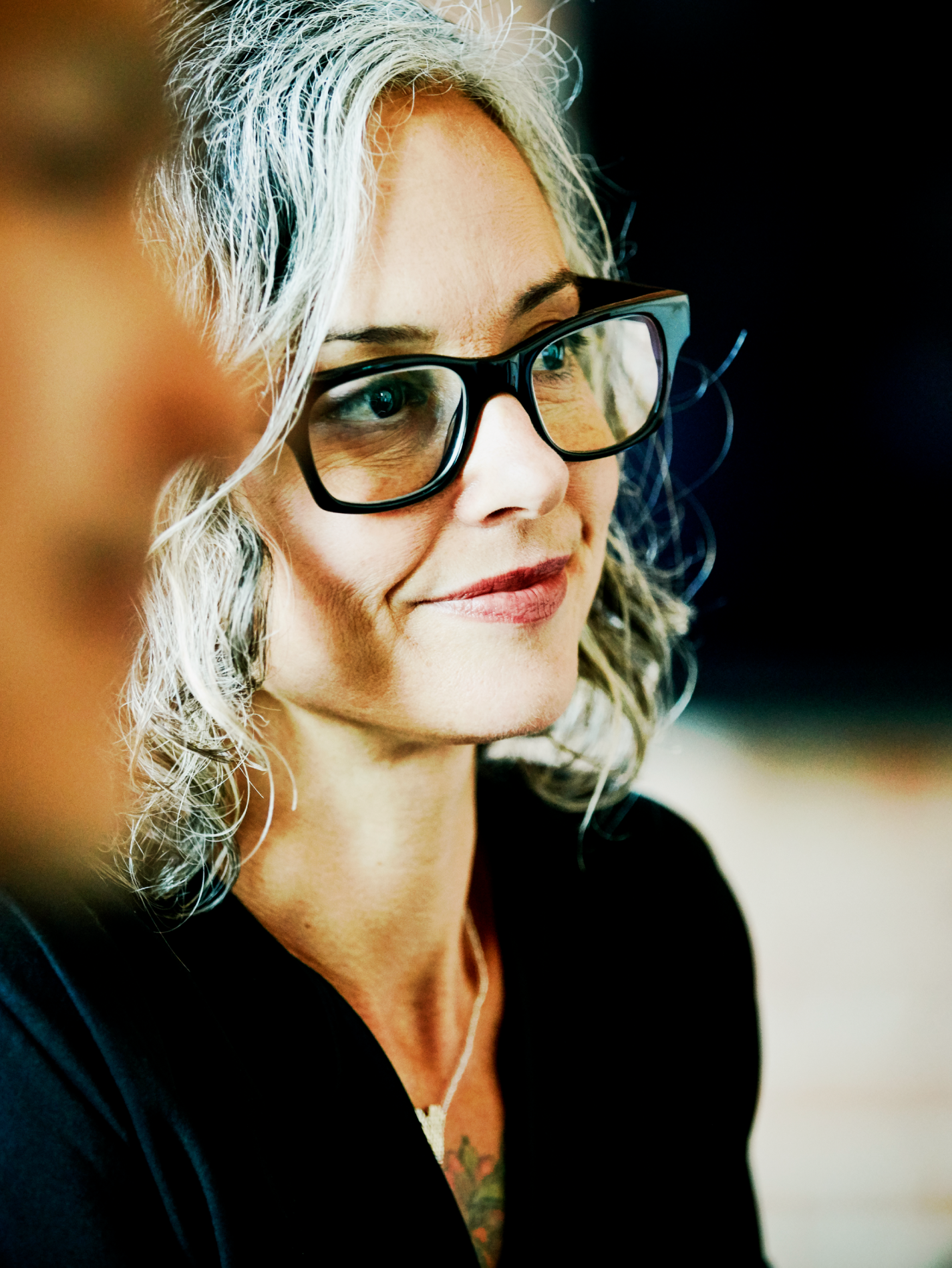 Close-up portrait of a woman with gray hair and black glasses, looking slightly to the side.