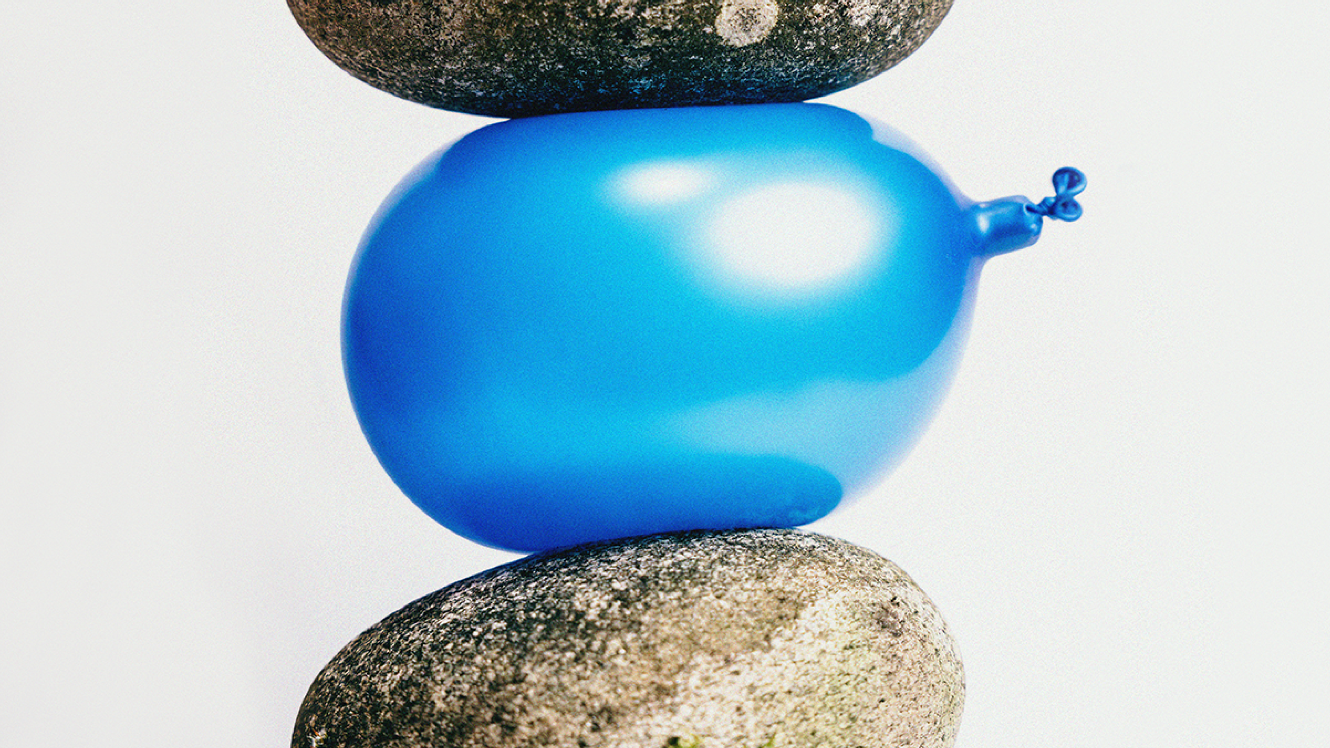 A photograph of a blue balloon squeezed between two stones