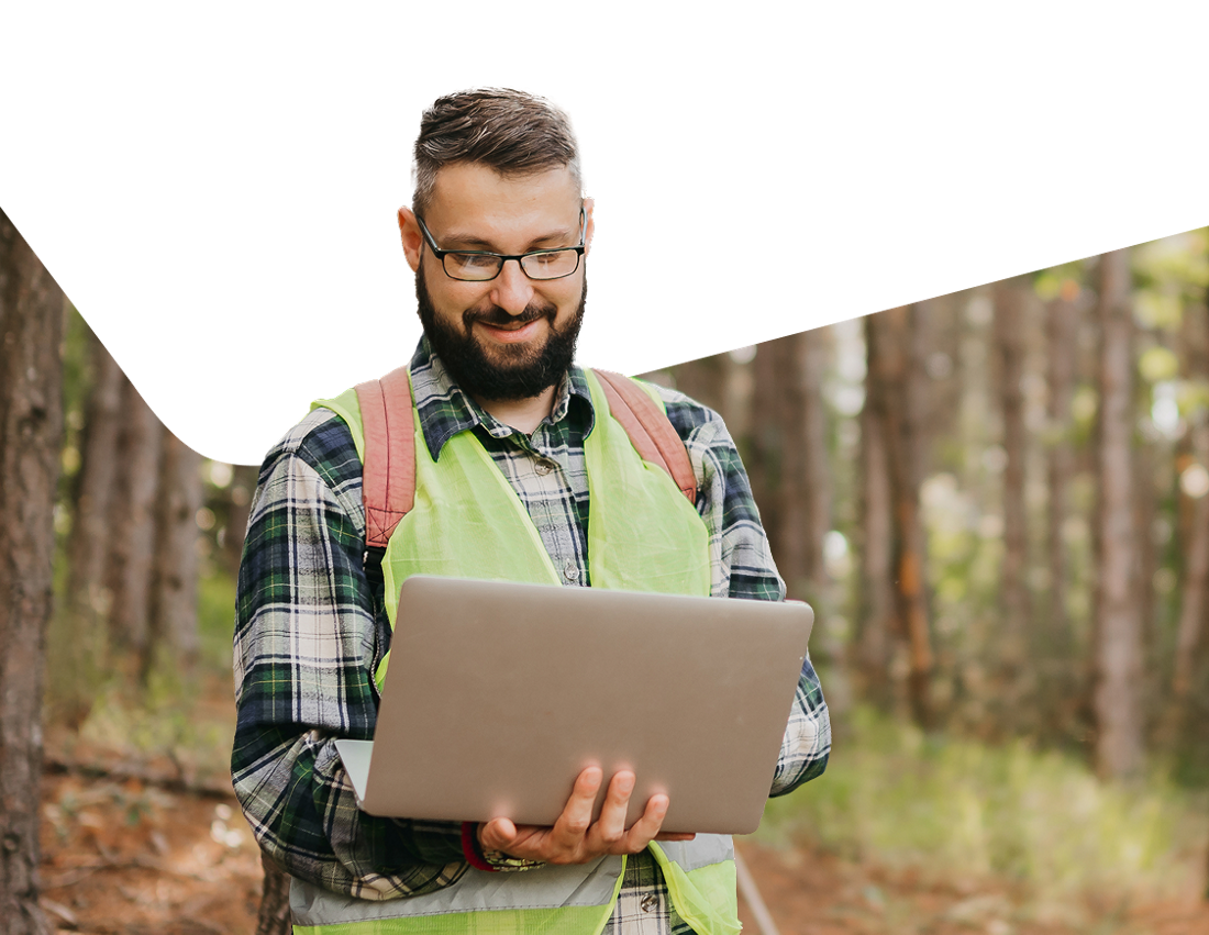 Photo d’un employé de l’industrie forestière dans la forêt consultant les solutions de Banque Nationale sur son ordinateur