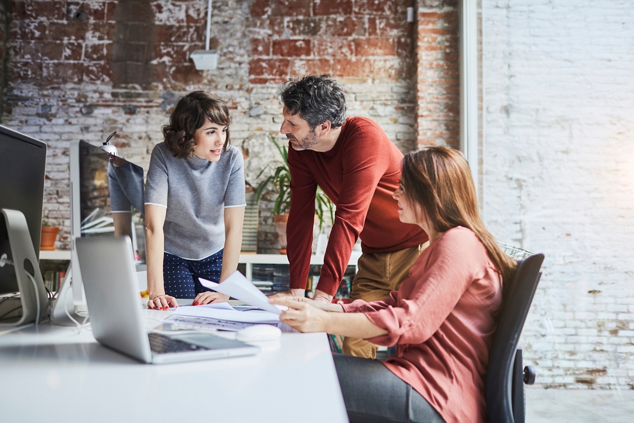 Photo of three people speaking at a desk representing the need to prepare your business to withstand a recession 