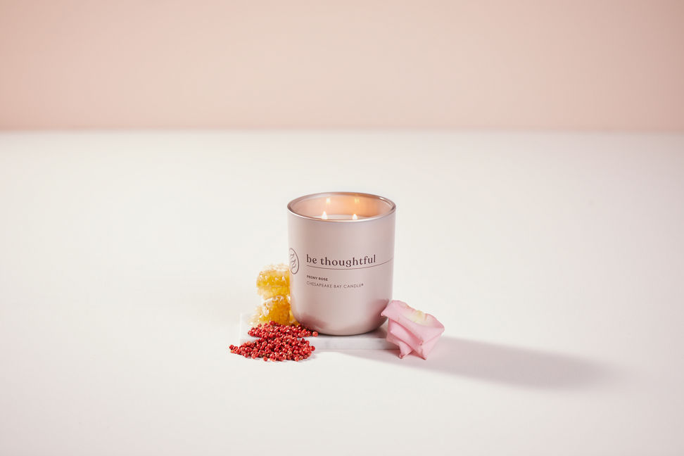 chesapeake bay candle intentions collection be thoughtful peony rose medium two wick jar candle surrounded by berries, pink petals, and honey in a pastel pink backdrop