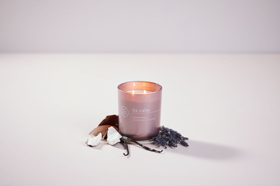 chesapeake bay candle intentions collection be calm coconut santal medium two wick jar candle surrounded by coconut pieces in a pastel purple backdrop