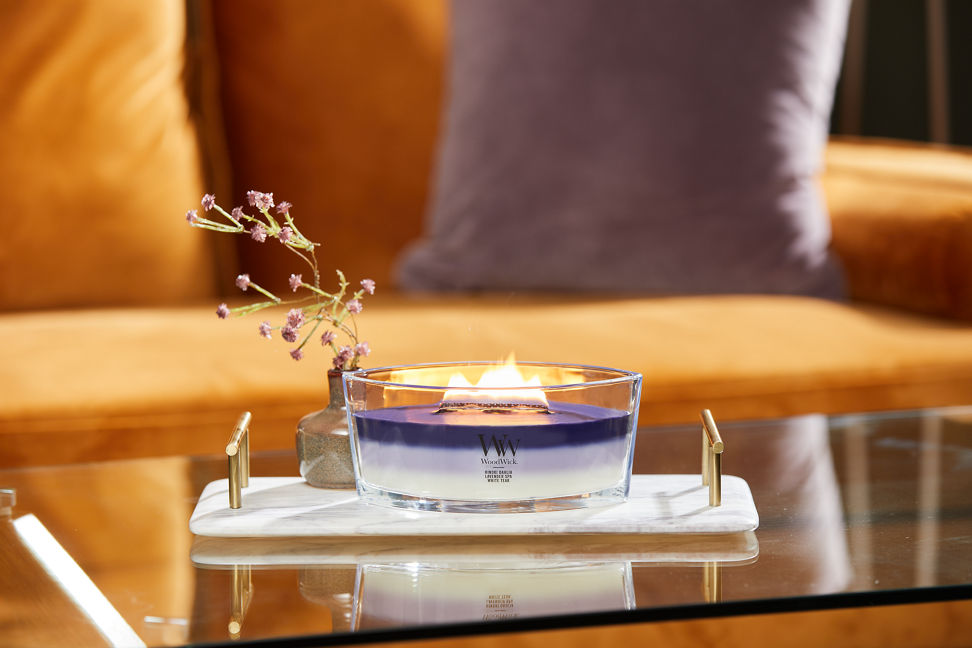 purple trilogy ellipse candle on stone tray with small bottle of flowers on glass coffee table