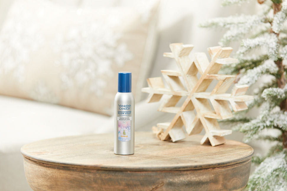 snow globe wonderland concentrated room spray on a wood table next to a wood-carved snowflake