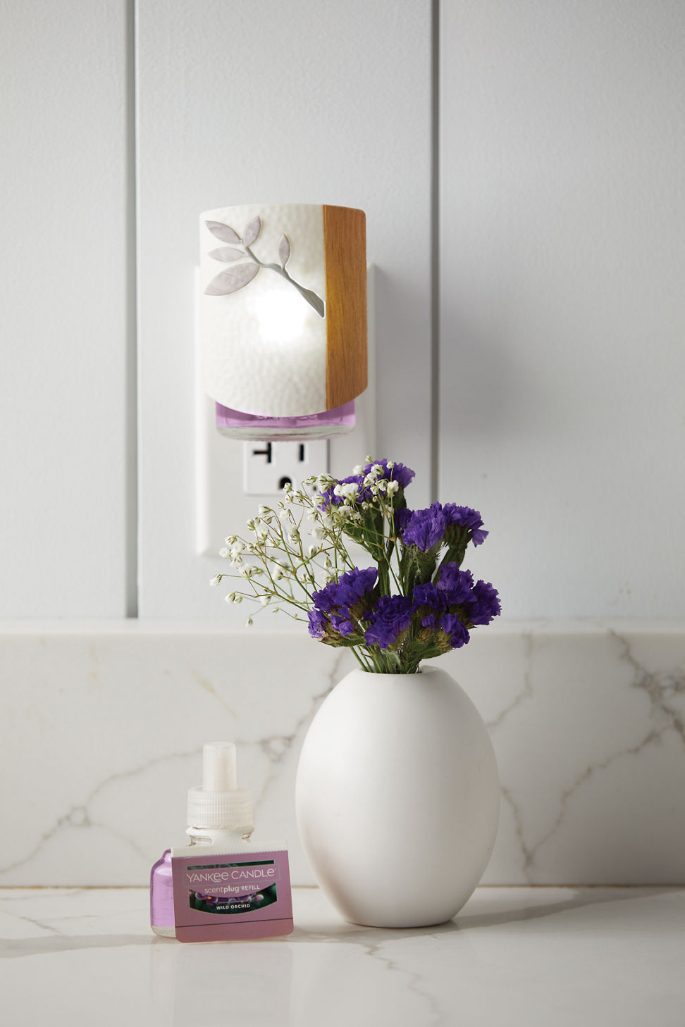two wild orchid scentplug refills and a dogwood scentplug diffuser next to a vase of purple and white flowers