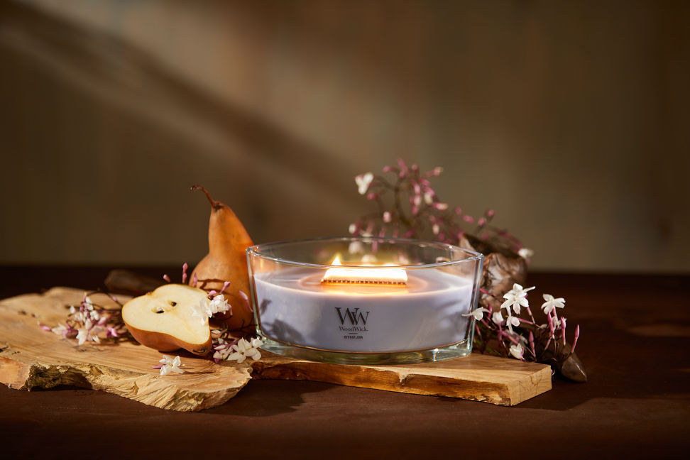 WoodWick Enchanted Destinations Collection Hypnoflora Ellipse Candle on a table with flowers and pears