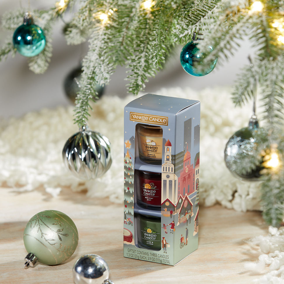 Holiday Party Minis Gift Set featuring a Vanilla Cupcake Yankee Candle Mini, a Holiday Zest Yankee Candle Mini, and a Sage & Citrus Yankee Candle Mini on a table surrounded by ornaments hanging on a tree