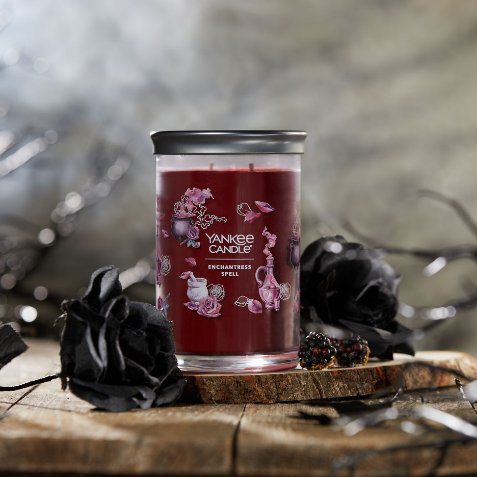 Enchantress Spell Signature Large Tumbler Candle next to two black roses on a piece of wood
