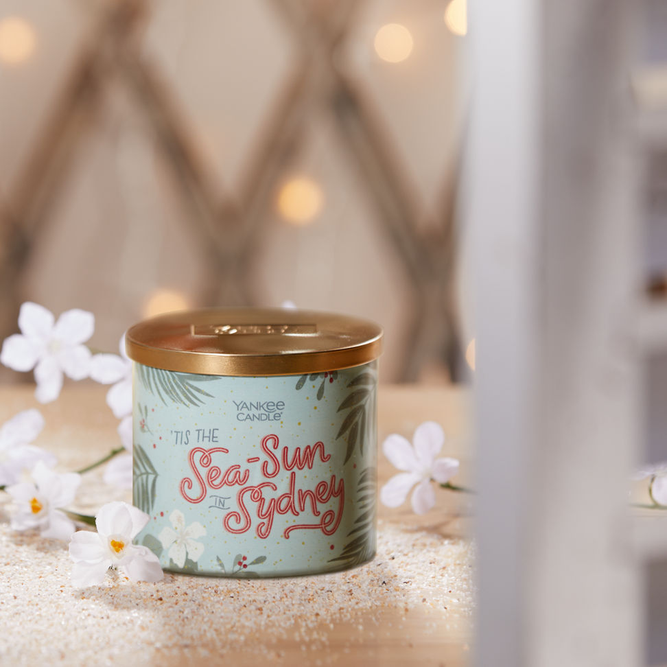 tis the sea-sun in sydney three wick candle on table with white flowers and sand