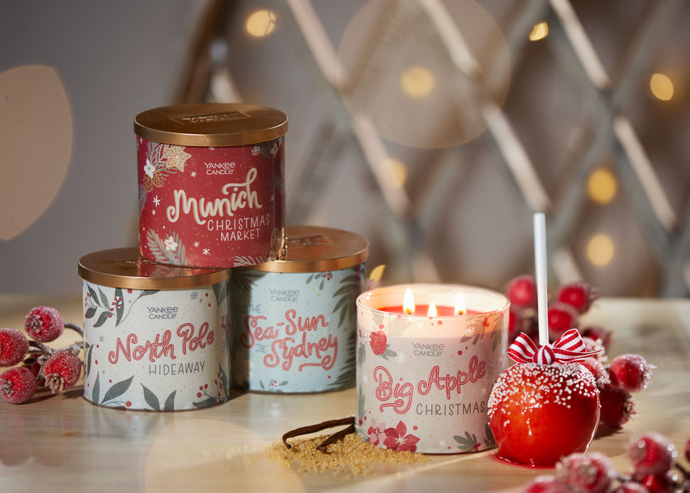 four three wick candles in passport to the holidays scents with a candy apple, red berries, vanilla beans, and brown sugar