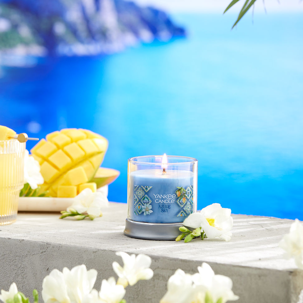 Hello, Italy! Collection Azure Sky Signature Small Tumbler Candle next to white flowers, sliced fruit, and a mixed drink