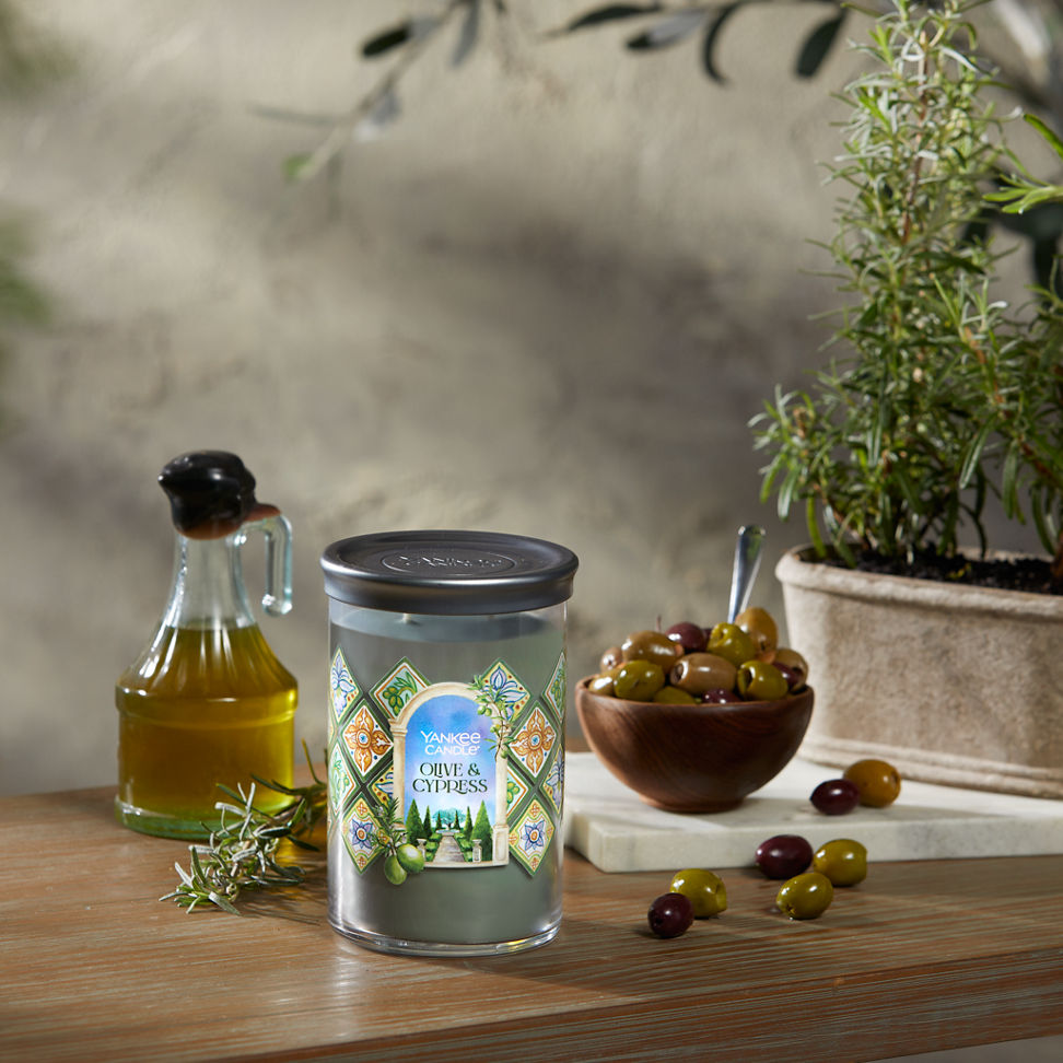Hello, Italy! Collection Olive & Cypress Signature Large Tumbler Candle on a table with a jar of olive oil and a bowl of olives