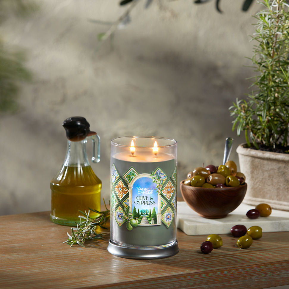 Hello, Italy Collection Olive & Cypress Signature Large Tumbler Candle on a table with a jar of olive oil and a bowl of olives