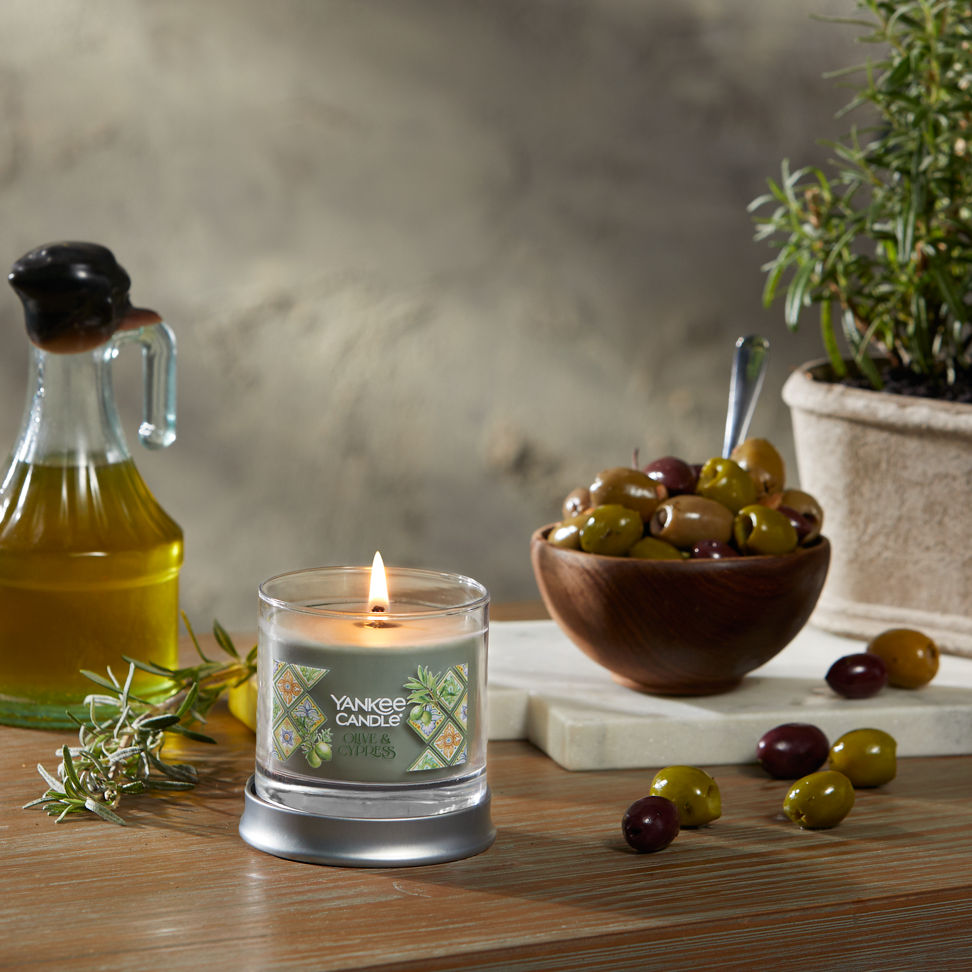 Hello, Italy! Collection Olive & Cypress Signature Small Tumbler Candle on a table with a bowl of olives and a jar of olive oil