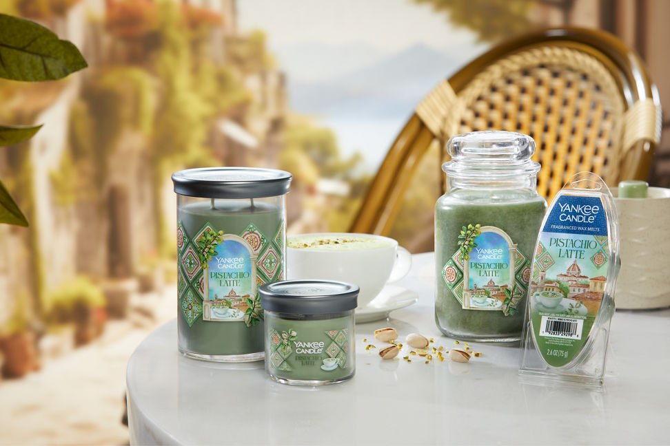 Hello, Italy! Collection Pistachio Latte Signature Large Tumbler Candle, a Pistachio Latte Signature Small Tumbler Candle, a Pistachio Latte Original Large Jar Candle, a Sandstone Wax Warmer, and Pistachio Latte Wax Melts (6-Pack) on a table with a latte and pistachios