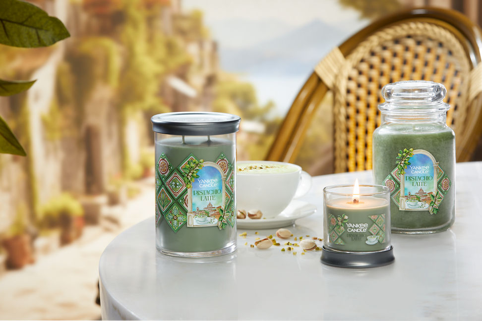 Hello, Italy! Collection Pistachio Latte Signature Large Tumbler Candle, Pistachio Latte Signature Small Tumbler Candle, and Pistachio Latte Original Large Jar Candle on a table with pistachios and a latte